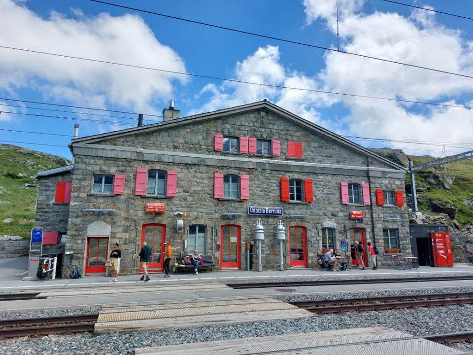 Ospizio Bernina station building at 2,253m — stone facade with red shutters and the railway platform in the foreground